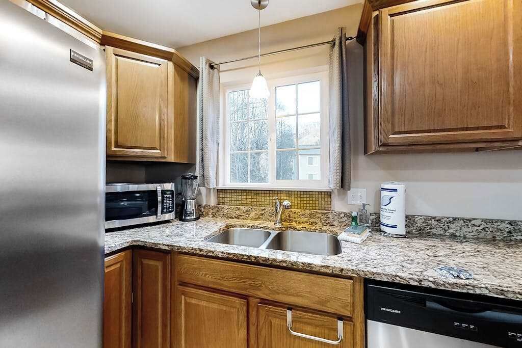 A kitchen with wooden cabinets, a stainless steel refrigerator, a microwave, a sink, and a dishwasher.