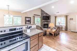 A kitchen with a built-in stove, a stone fireplace, and a dining area with a sofa and table. - Full Steam Ahead (Whittier)