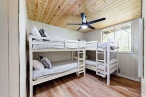 A bunk bed room with a ceiling fan, wooden walls, and a window. - Nantahala Lake Hideout (Topton)