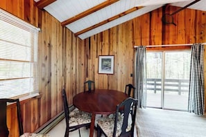 A wooden-paneled room with a round table and chairs, a framed picture on the wall, and a sliding glass door to the outside. - Nantahala Lake Hideout (Topton)