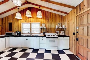 A kitchen with wooden walls, white cabinets, a black and white checkered floor, and pendant lights. - Nantahala Lake Hideout (Topton)