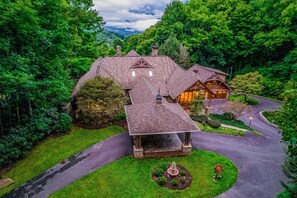 A large house with a covered porch, surrounded by lush greenery and a winding driveway. - Spectacular Wooded Estate W/ Private Hot Tub, Veranda & Pool Table (Waynesville)