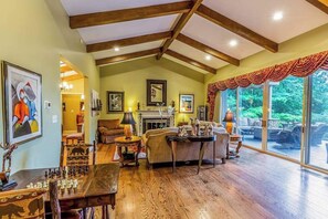 A spacious living room with a fireplace, wooden floors, and large windows. - Spectacular Wooded Estate W/ Private Hot Tub, Veranda & Pool Table (Waynesville)