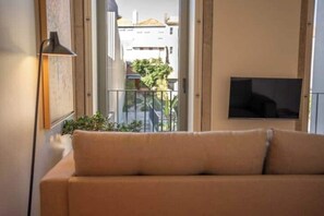 A living room with a sofa, a TV mounted on the wall, and a balcony with a railing. - 4. Deluxe Suite (Garden View) (Porto)