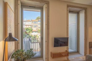A room with a TV, a plant, and a balcony with a view of buildings. - 4. Deluxe Suite (Garden View) (Porto)