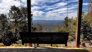 A wooden bench with a stone floor, surrounded by trees and a mountainous landscape. - The Ridge House (Franklin)