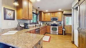 A kitchen with granite countertops, wooden cabinets, stainless steel appliances, and pendant lighting. - The Ridge House (Franklin)