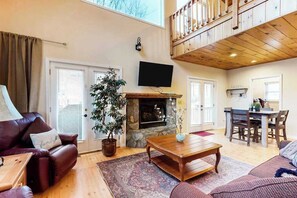 Ein Wohnzimmer mit Kamin, Fernseher, Essbereich und Balkon.