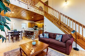 Ein ger äumiger Wohnbereich mit einer Holztreppe, einem Esstisch, einer Couch und einer Küche im Hintergrund.