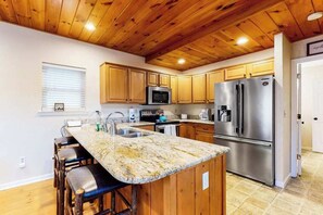 Eine Küche mit Holzausstattung, einem Edelstahl-Kühlschrank, einer Mikrowelle und einer Arbeitsplatte aus Granit.