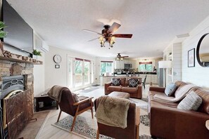 Ein großzügiges Wohnzimmer mit Kamin, Deckenventilator und einer Küche im Hintergrund.
