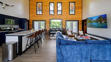 A spacious interior with a kitchen, dining area, and living room, featuring wooden walls, large windows, and a central island.