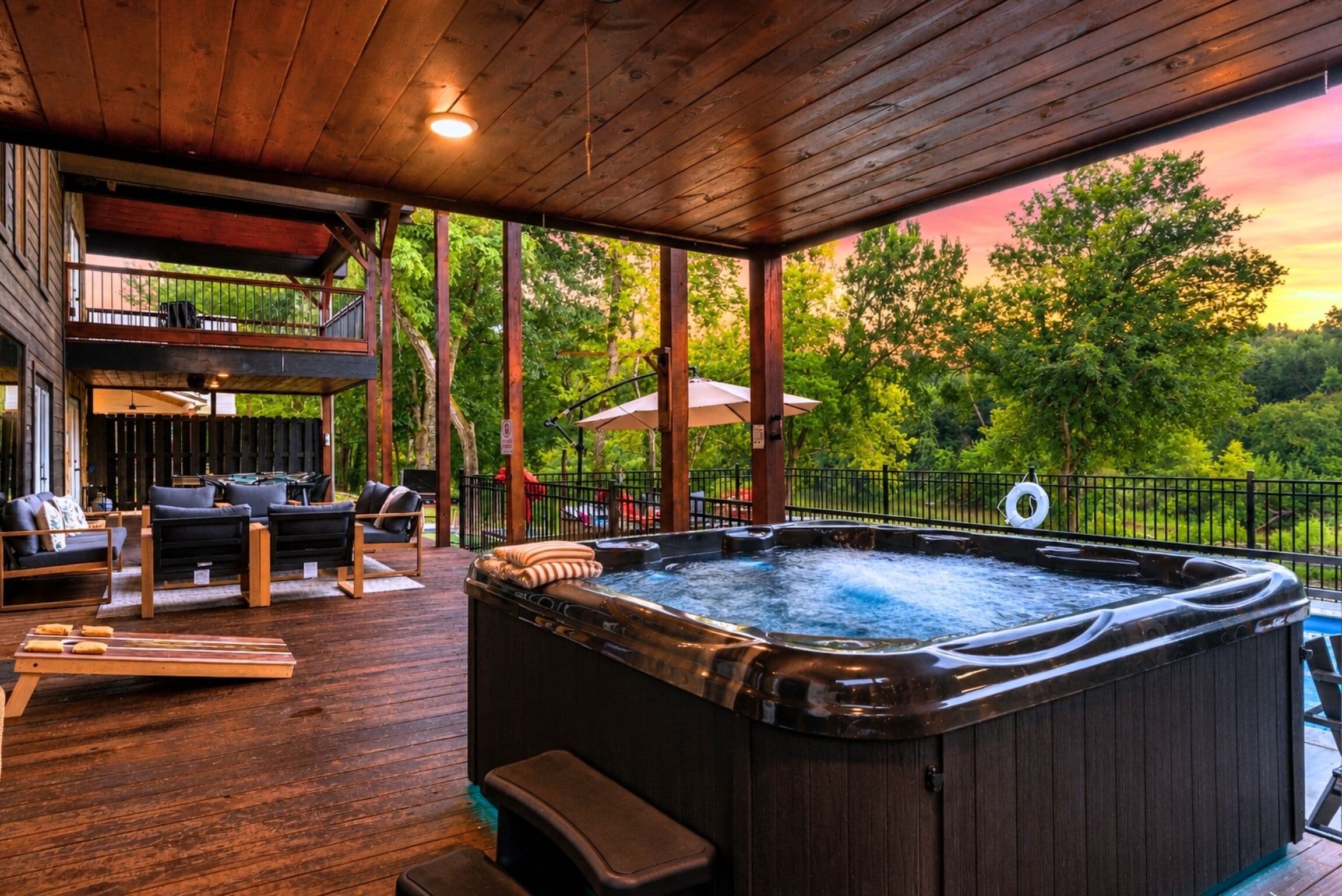 A hot tub on a wooden deck with outdoor furniture and a view of trees.