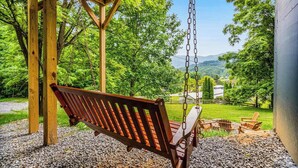 Ein Spielplatz mit Holzschaukeln, einer Sitzbank, einem Feuerkorb und Blick auf eine grüne Landschaft.