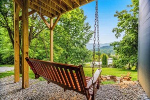 A wooden swing set with a bench, a fire pit, and a view of a green landscape. - Inviting home with enclosed yard, mountain view, firepit, & W/D (Waynesville)