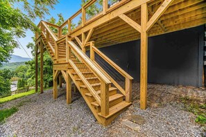 A wooden staircase leading to a building with a modern design, surrounded by a gravel area and greenery. - Inviting home with enclosed yard, mountain view, firepit, & W/D (Waynesville)