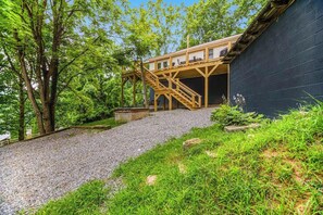 A building with a wooden staircase leading to a deck, surrounded by trees and a gravel path. - Inviting home with enclosed yard, mountain view, firepit, & W/D (Waynesville)