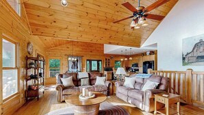 A spacious living room with wooden floors, leather sofas, a coffee table, and a ceiling fan. - The Glens of Iron Duff (Waynesville)