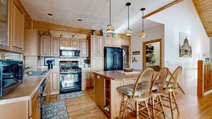A kitchen with wooden cabinets, a refrigerator, an oven, and a dining area with chairs. - The Glens of Iron Duff (Waynesville)