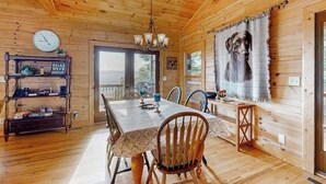 A wooden cabin interior with a dining table, chairs, a chandelier, a clock, and a large painting of a dog. - The Glens of Iron Duff (Waynesville)