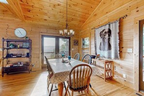 Ein Holzblockhaus-Interieur mit Esstisch, Stühlen, einer Pendelleuchte, einer Uhr und einem großen Gemälde von einem Hund.