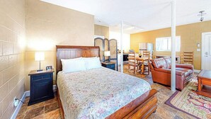 Een hotelkamer met een bed, nachtkastje, lamp, houten hoofdeinde en een zithoek met een bank en stoelen.