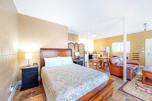A hotel room with a bed, bedside table, lamp, wooden headboard, and a seating area with a sofa and chairs. - Cozy Mountain Hideaway (Waynesville)