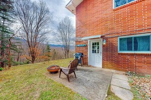 A brick house with a front door, a window, and a patio with a chair and a bowl. - Cozy Mountain Hideaway (Waynesville)
