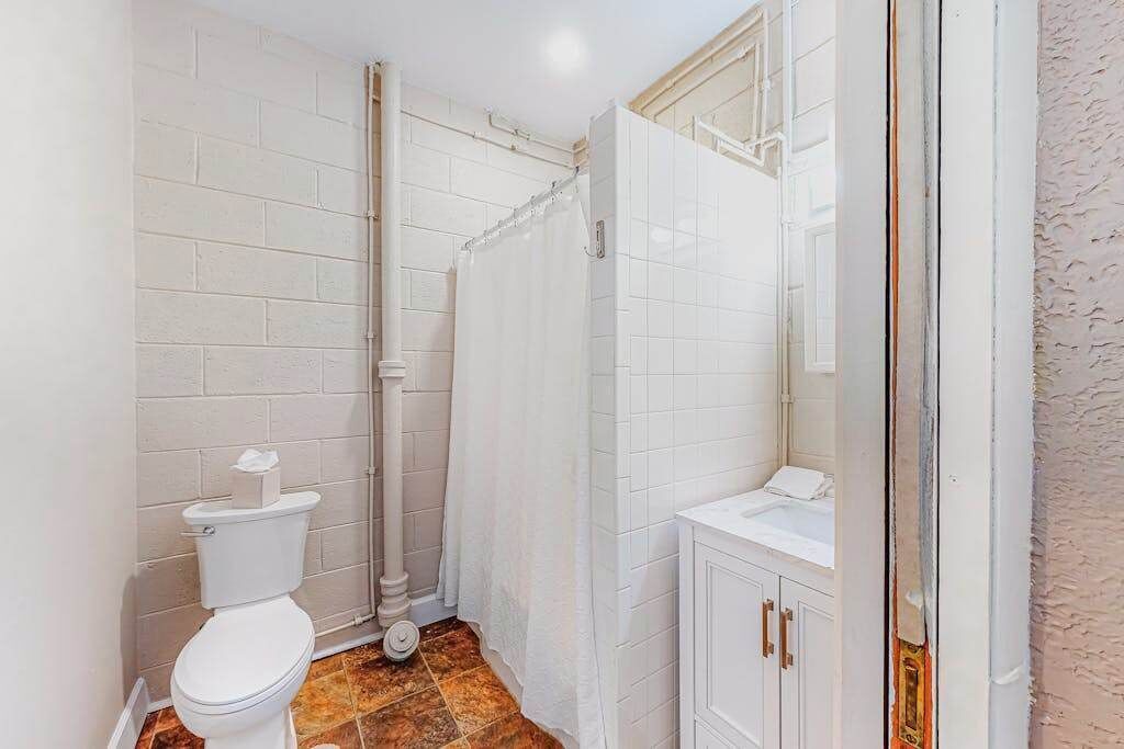 A bathroom with white tiled walls, a white toilet, a shower curtain, and a sink with a cabinet.