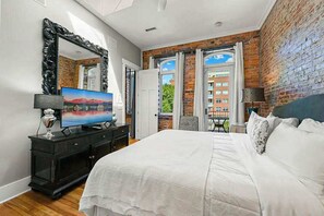 Ein Schlafzimmer mit einem großen Bett, einem Fernseher, einem Schminktisch und einer Ziegelwand.