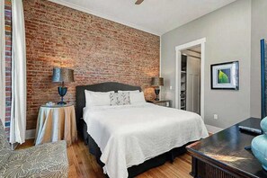 Ein Schlafzimmer mit Ziegelwand, einem Bett mit weißer Bettwäsche, einem Nachttisch mit Lampe und einem gerahmten Bild an der Wand.