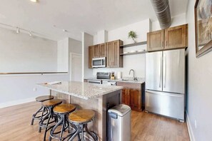 A modern kitchen with a central island, bar stools, stainless steel appliances, wooden cabinets, and a microwave. - Spacious, chic retreat with balcony & AC - walk to dining & shopping (Asheville)