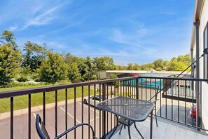 A balcony with a metal railing, a table, and chairs, overlooking a parking lot and a swimming pool. - Spacious, chic retreat with balcony & AC - walk to dining & shopping (Asheville)