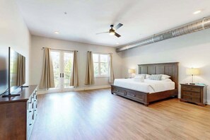 A spacious bedroom with a large bed, a ceiling fan, a TV, and a wooden dresser. - Spacious, chic retreat with balcony & AC - walk to dining & shopping (Asheville)