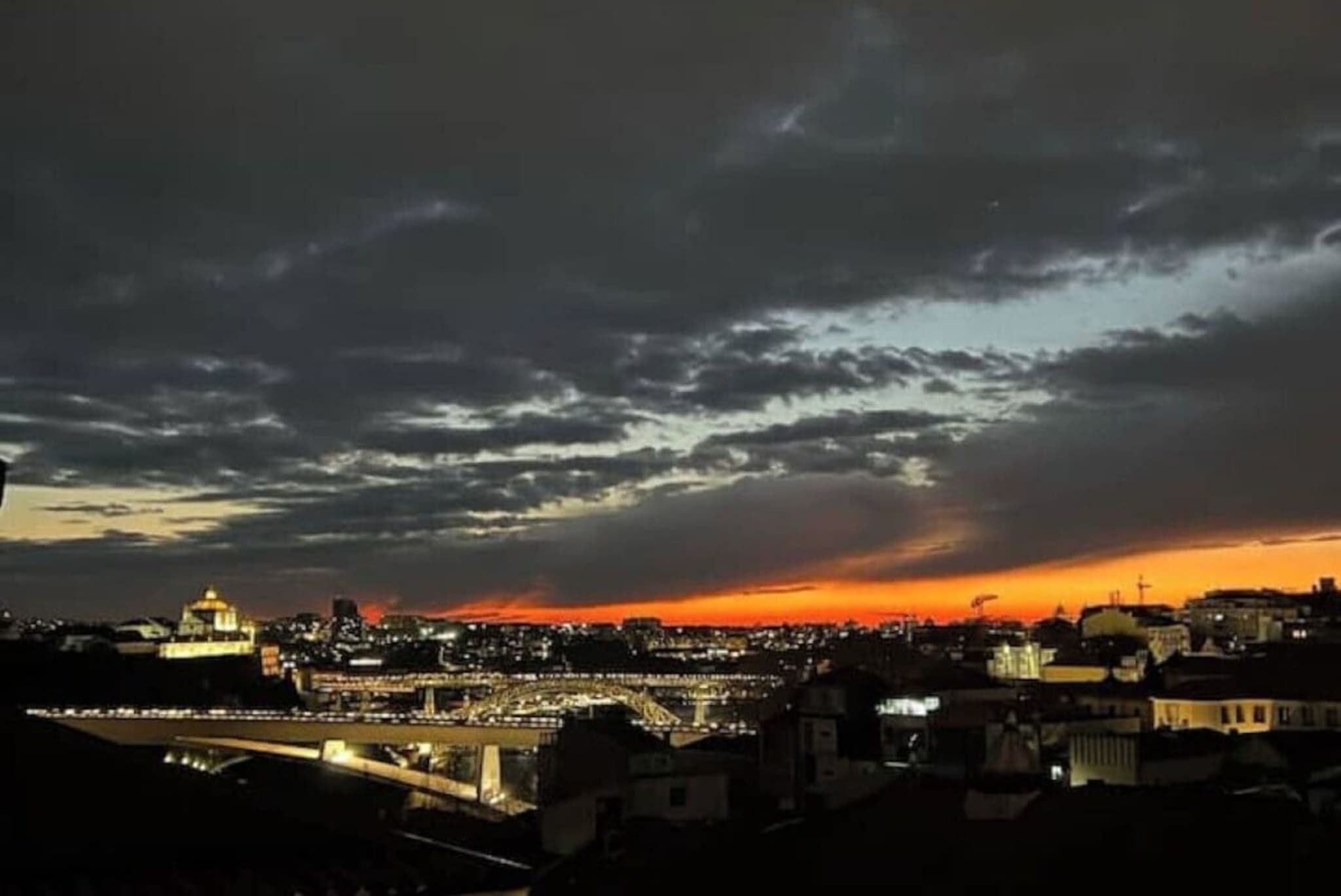 A cityscape at dusk with illuminated buildings and a bridge.