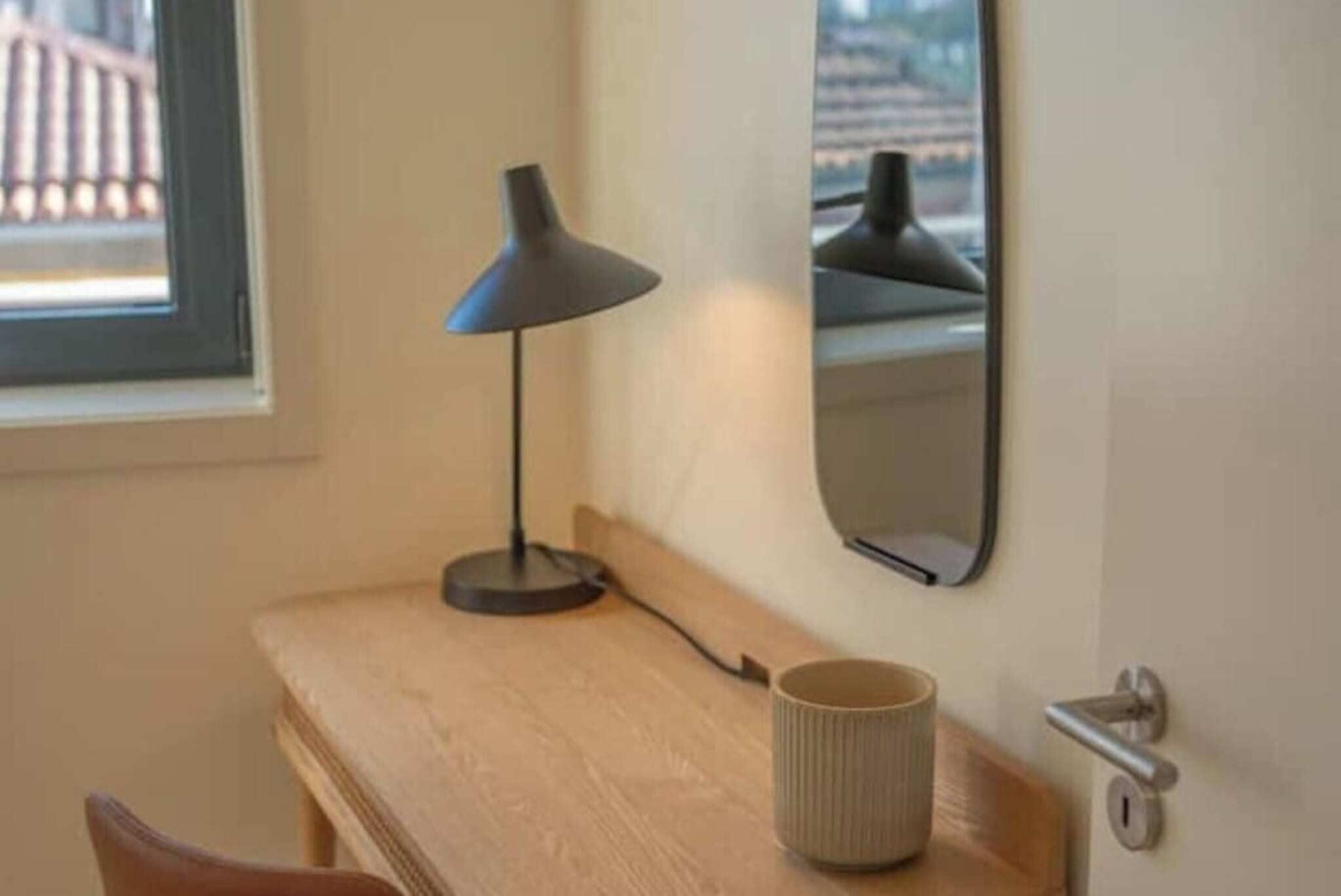 Un escritorio de madera con una lámpara, una taza y una puerta con manija.