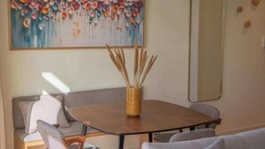 Un coin repas avec une table ronde, des chaises, un panier tressé en roseaux, un canapé et un tableau abstrait aux couleurs vives accroché au mur.