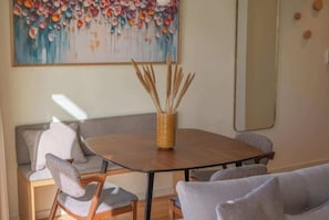 A dining area with a round table, chairs, a woven basket with reeds, a sofa, and a colorful abstract painting on the wall. - 3. Deluxe Suite (River and City View) (Porto)