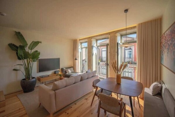 A modern living room with a sofa, dining table, and a TV. - 3. Deluxe Suite (River and City View) (Porto)