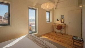 Une chambre à coucher avec un lit, un bureau, une chaise, une fenêtre et une vue sur l’extérieur.