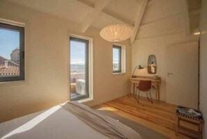 A bedroom with a bed, a desk, a chair, a window, and a view of the outside. - 3. Deluxe Suite (River and City View) (Porto)