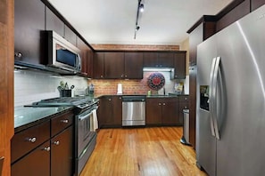 A modern kitchen with dark wooden cabinets, stainless steel appliances, and a brick backsplash. - #102 - The Lofts at Church Street (Asheville)