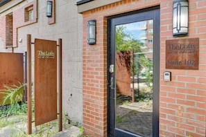A hotel entrance with a brick facade, a black door, and signage indicating 'The Lofts at 16 Church' and 'Suite 102.' - #102 - The Lofts at Church Street (Asheville)