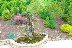Ein Garten mit einem kleinen Wasserfall, verschiedenen Sträuchern und einer Steingrenze.