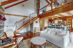 Ein großzügiger Wohnbereich mit einer Holztreppe, einem weißen Sofa und einer Küche im Hintergrund.