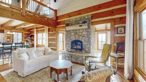 Una sala de estar amplia con chimenea de piedra, vigas de madera, un sofá blanco y un comedor.
