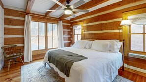 Un dormitorio tipo cabaña de troncos con una cama, un ventilador de techo, un banco y ventanas grandes.