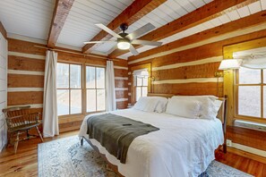 Ein Schlafzimmer in einer Blockhütte mit einem Bett, einem Deckenventilator, einer Bank und großen Fenstern.