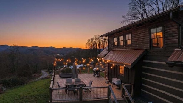Una cabaña de madera con terraza, muebles de exterior e iluminación con luces colgantes.