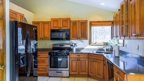 A kitchen with wooden cabinets, a refrigerator, a microwave, an oven, and a sink. - Meadow Creek Manor (Whittier)